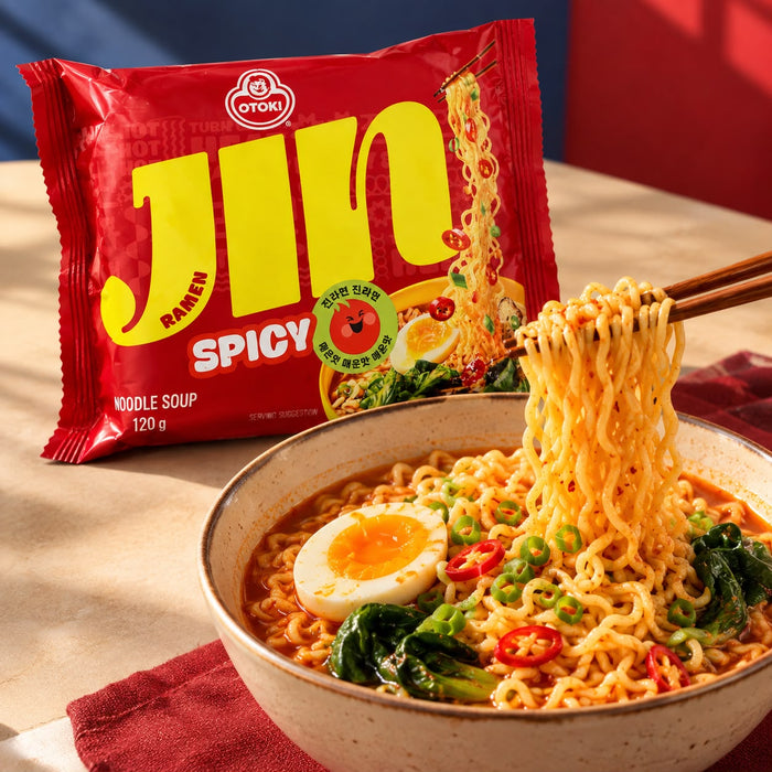 Jin Ramen Spicy packet beside a bowl of noodles topped with egg, greens and sliced chillies.
